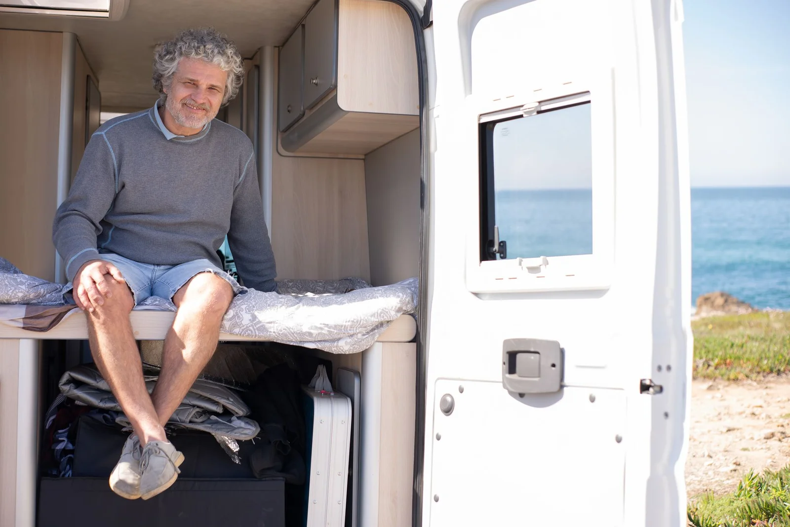 Mann sitzt in der geöffneten Hecktür eines ausgebauten Campervans mit Einbaumöbeln