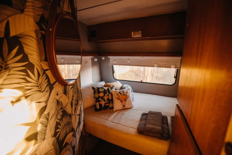 Warm beleuchteter Camper-Innenraum mit Bett, Holzmöbeln und geöffnetem Seitenfenster