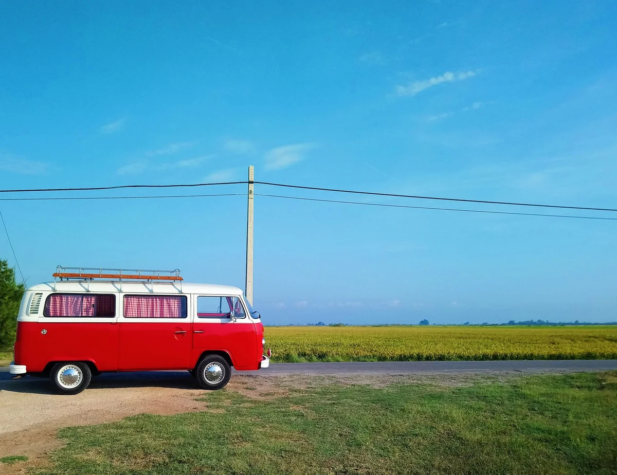Roter Volkswagen Camper auf einer hellen Landstraße am Feld