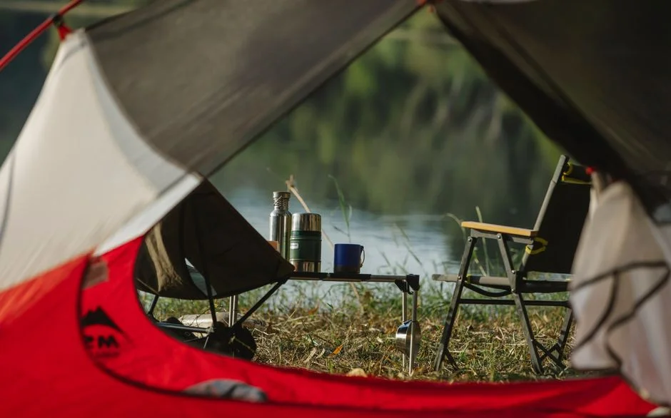 Zelt mit Campingstühlen an einem Flussufer im warmen Licht
