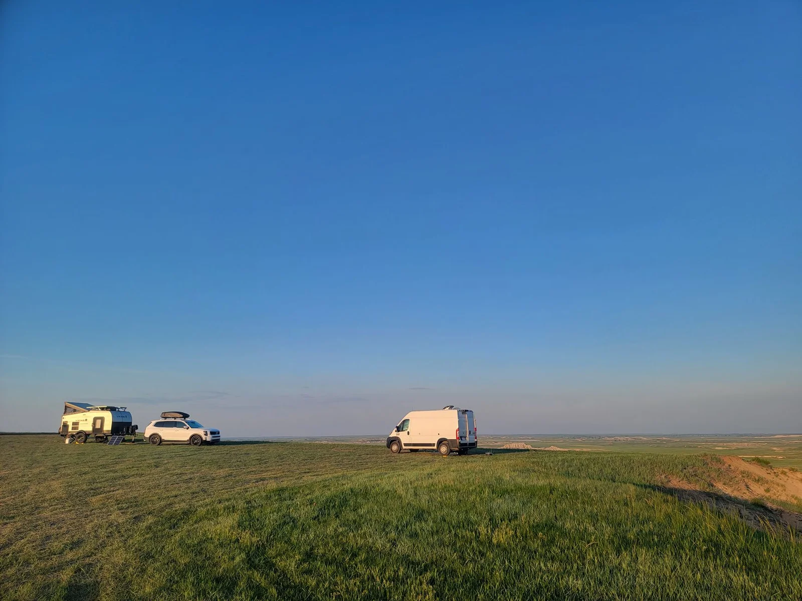 Kastenwagen und Wohnanhänger stehen bei blauem Himmel frei auf einer Wiese
