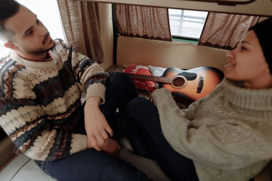 Zwei Personen sitzen in warmer Kleidung im Innenraum eines ausgebauten Campers