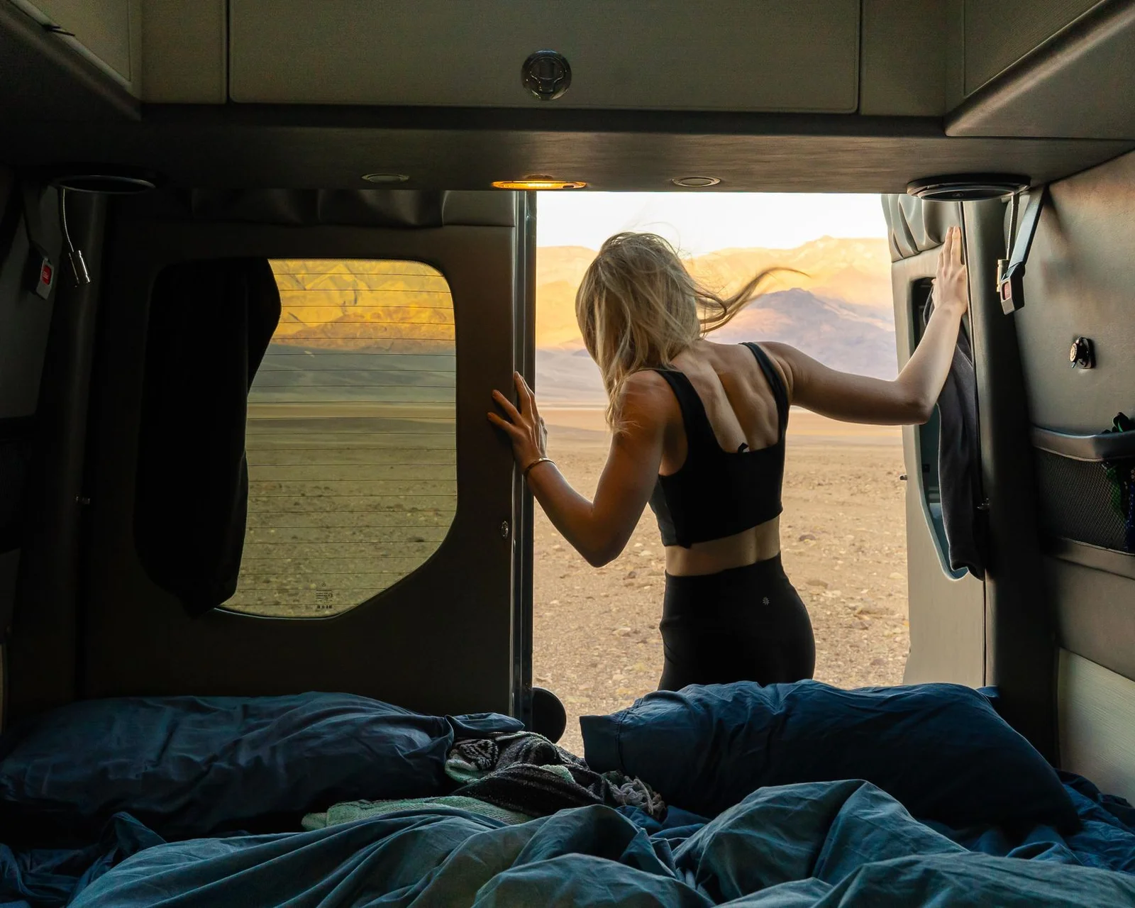 Blick vom Bett durch die geöffneten Hecktüren eines Vans in eine weite Landschaft