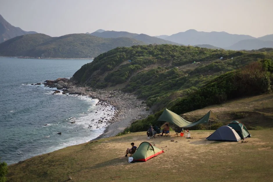 Camper und Zelte an einer sonnigen Küstenlandschaft mit Blick aufs Meer
