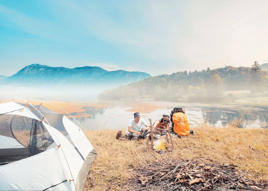 Camping am See im warmen Morgenlicht mit Zelt und kleiner Feuerstelle