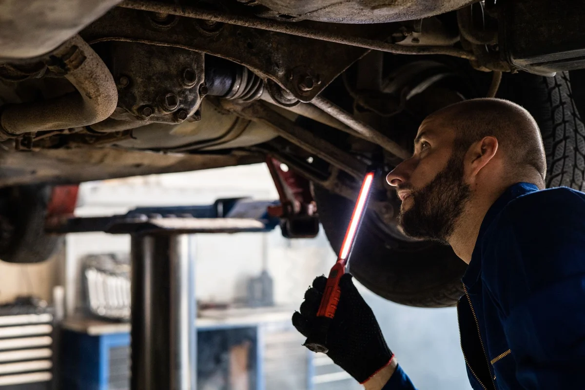 Mechaniker prüft die Unterseite eines Fahrzeugs in der Werkstatt