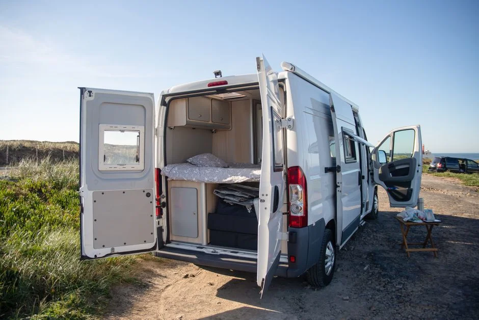 Kastenwagen-Camper mit geöffneten Hecktüren, Blick auf Bett und Möbelmodule des Ausbaus
