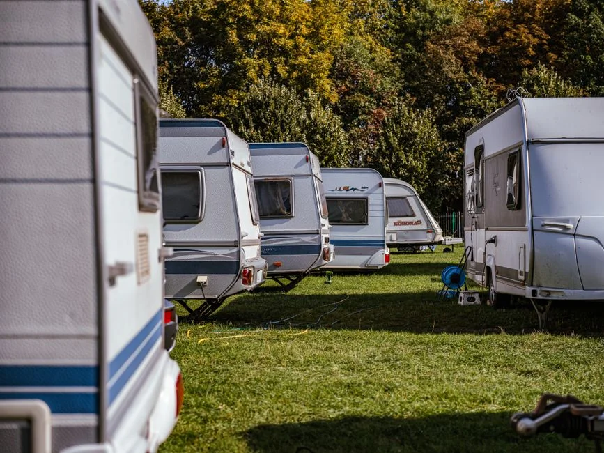 Mehrere Wohnwagen mit ausgefahrenen Stützen nebeneinander auf einer Campingwiese